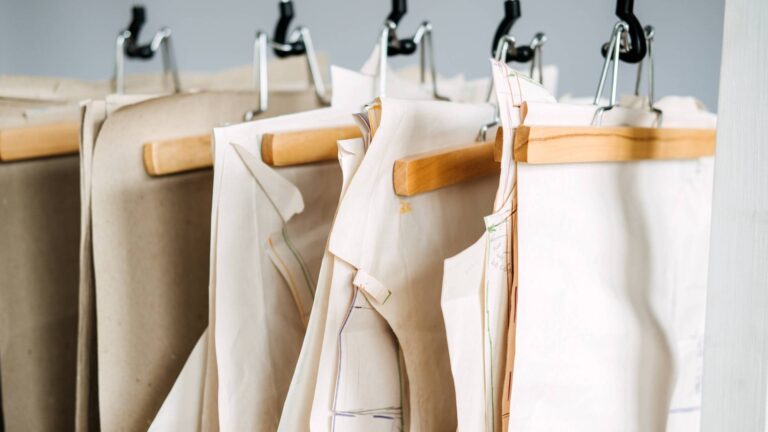 Many paper sewing patterns for different clothes hanging on the rack in sewing factory background. Clothing pattern, manufacture on sewing factory